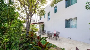 A courtyard with a white building, outdoor seating, and lush greenery. - Costa Norte Boutique Hotel (Miami Beach)