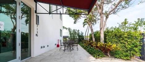 A modern building with a covered patio area, outdoor seating, and lush greenery.