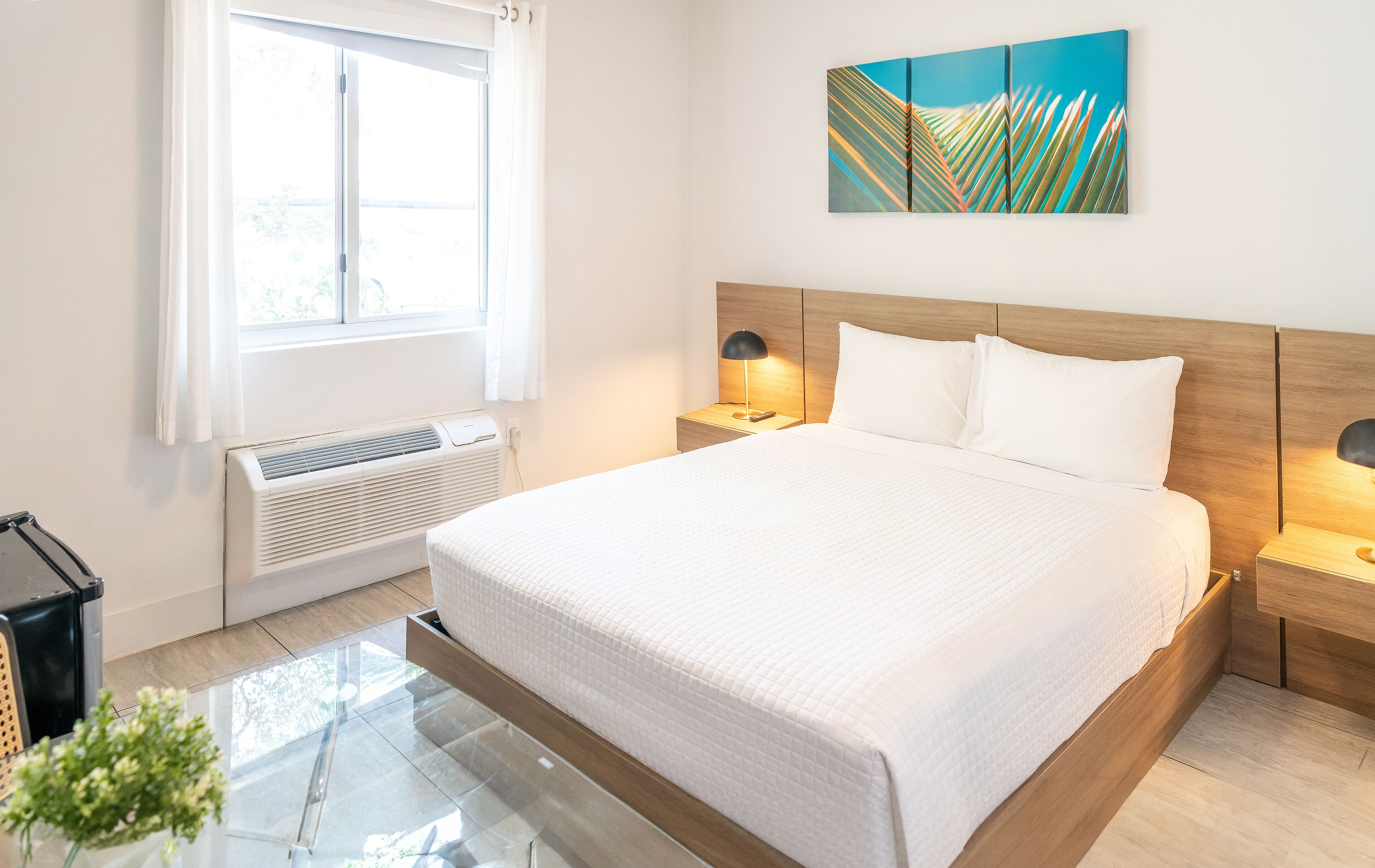Une chambre à coucher moderne avec un grand lit, des lampes de chevet, une œuvre d’art accrochée au mur et une fenêtre avec des rideaux.