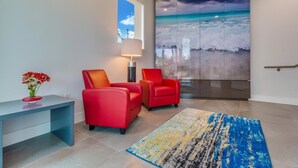 A modern room with a large window, a red sofa set, a blue desk, and a beach-themed artwork on the wall. - Costa Norte Boutique Hotel (Miami Beach)