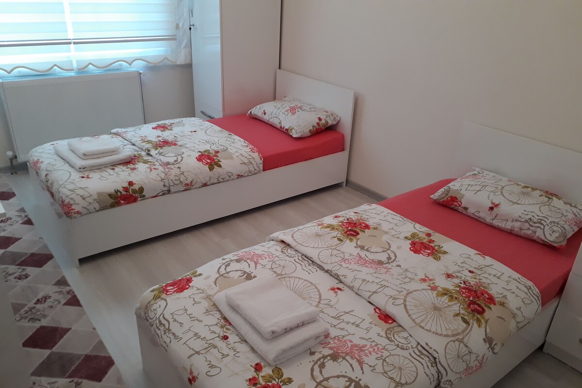Two single beds with floral bedding and red accents, a radiator, and a patterned floor.
