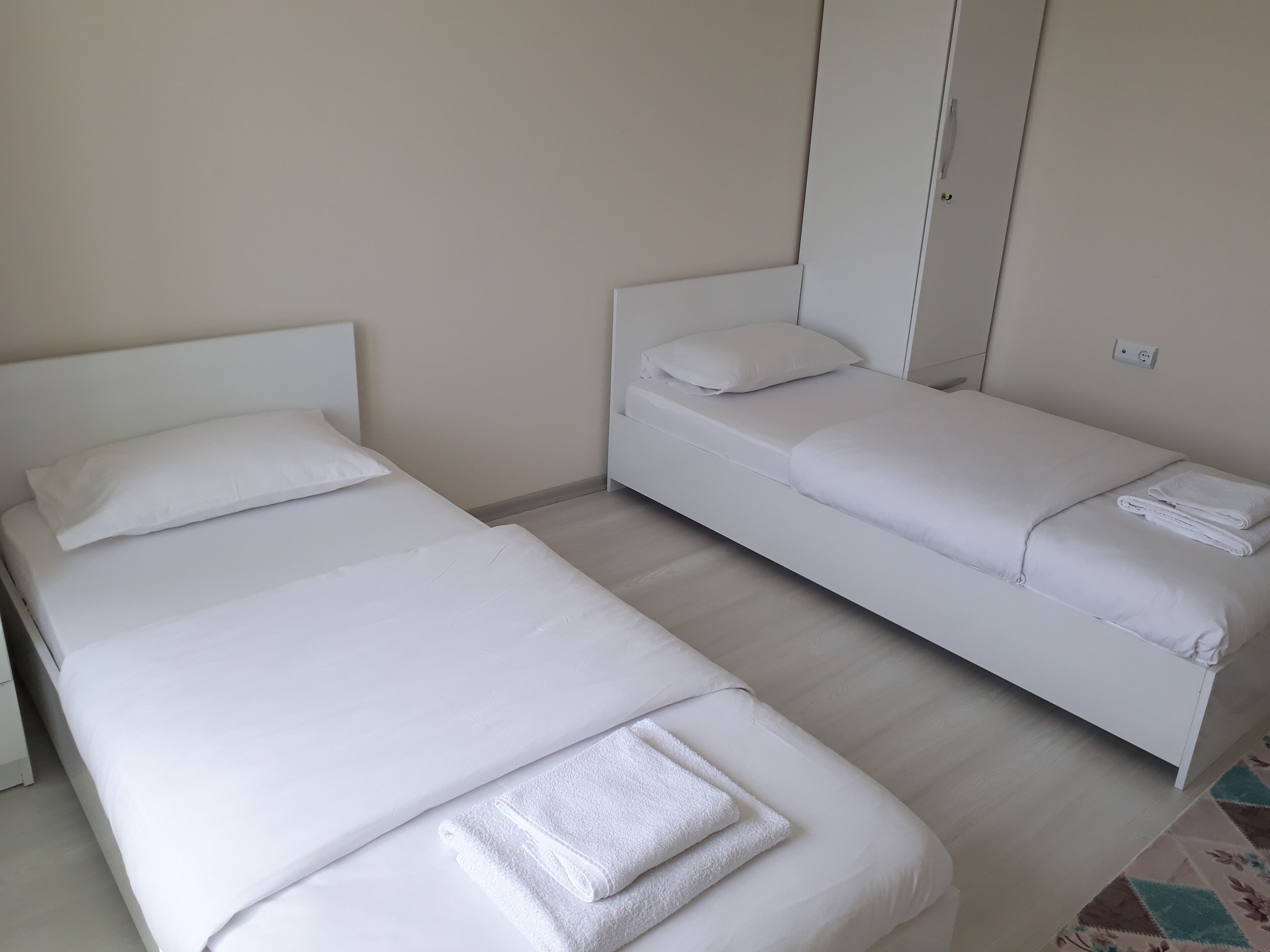 Duas camas de solteiro com roupa de cama e almofadas brancas, uma pequena mesa de cabeceira e uma tomada na parede.