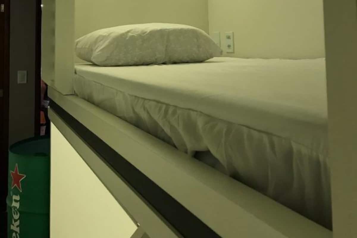 A bunk bed with a single mattress and pillow, a bedside table, and a wall-mounted light.