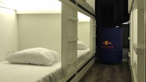 Un couloir étroit, avec des lits superposés de chaque côté, un réfrigérateur rempli de canettes de Red Bull et une porte sombre au fond.