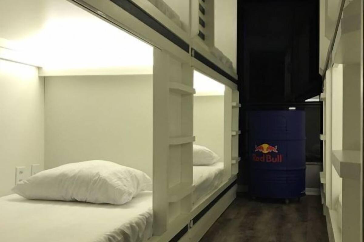A narrow hallway with bunk beds on either side, a Red Bull cooler, and a dark door at the end.