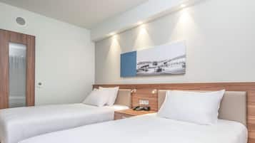 A hotel room with two single beds, a wooden headboard, a bedside table with a phone, and a wall-mounted picture.