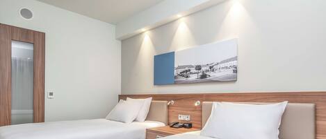 A hotel room with two single beds, a wooden headboard, a bedside table with a phone, and a wall-mounted picture.