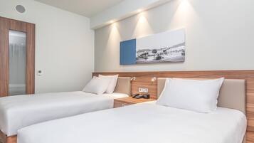 Quarto de hotel com duas camas, uma cabeceira de madeira, um criado-mudo com telefone e um quadro pendurado na parede.
