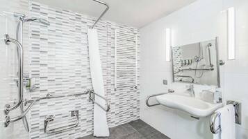 A modern bathroom with a shower, grab bars, a sink, and a mirror.
