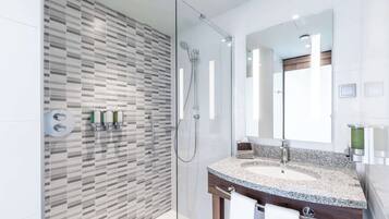 Une salle de bain moderne avec une douche à parois de verre, un grand miroir et un lavabo encastré dans un plan de travail en granit.