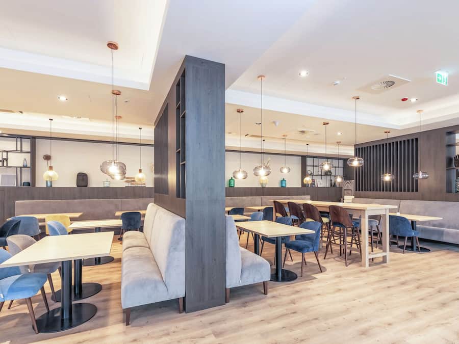 A modern restaurant with wooden flooring, blue and grey seating, and pendant lighting.