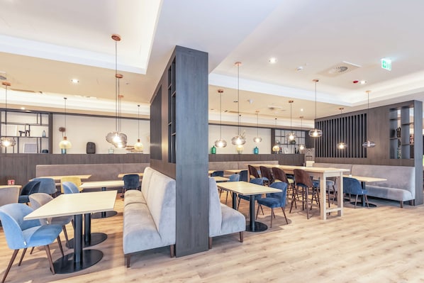 Un restaurante moderno con suelo de madera, asientos en tonos azul y gris, e iluminación colgante.