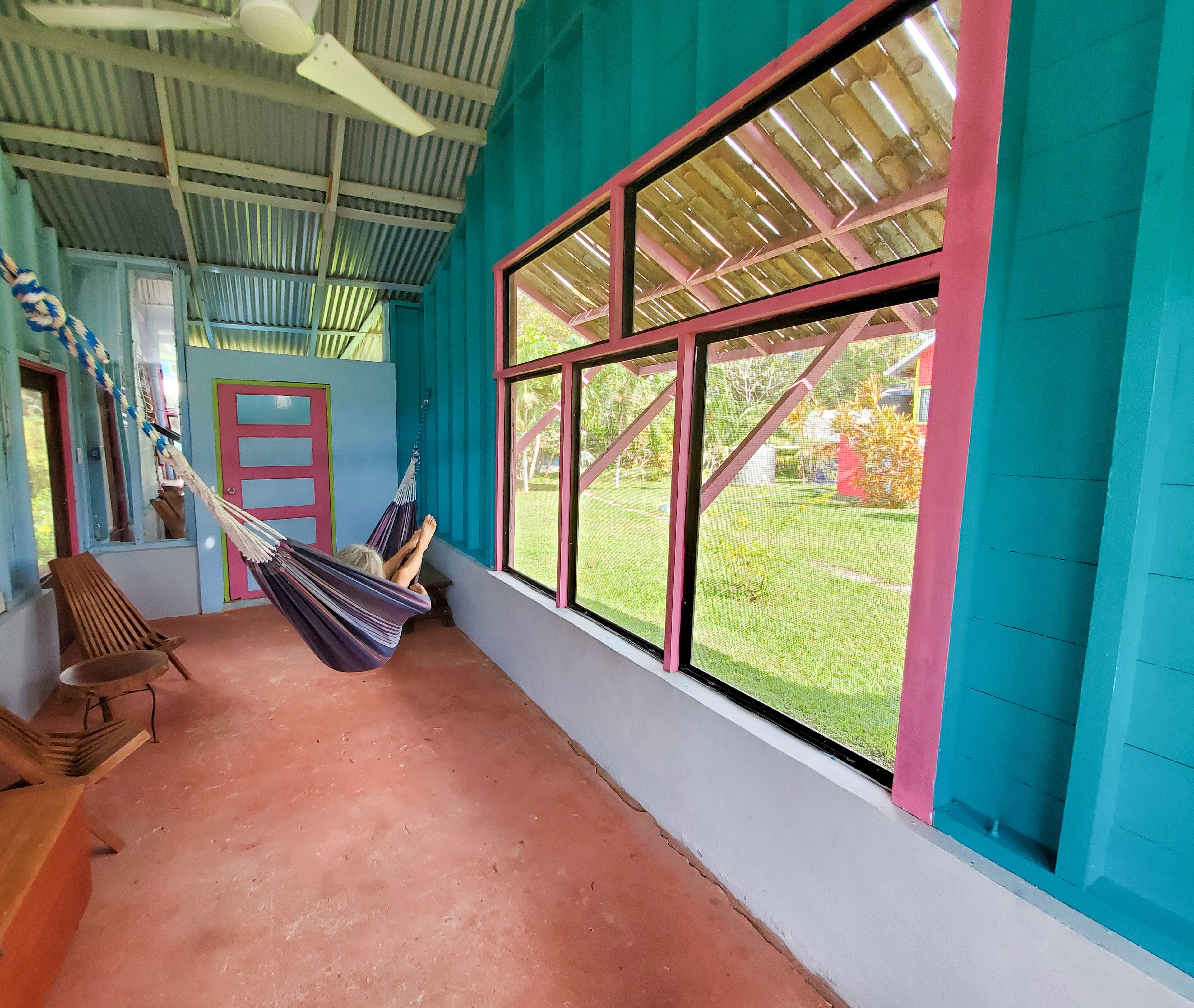 A room with a hammock, a wooden bench, and a large window with a view of a garden.