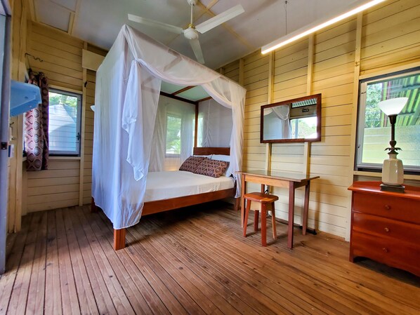 A bedroom with a canopy bed, a wooden desk, a dresser, a mirror, and a ceiling fan. - Lower Dover Jungle Lodge & Maya Ruins - Hostel (Unitedville)
