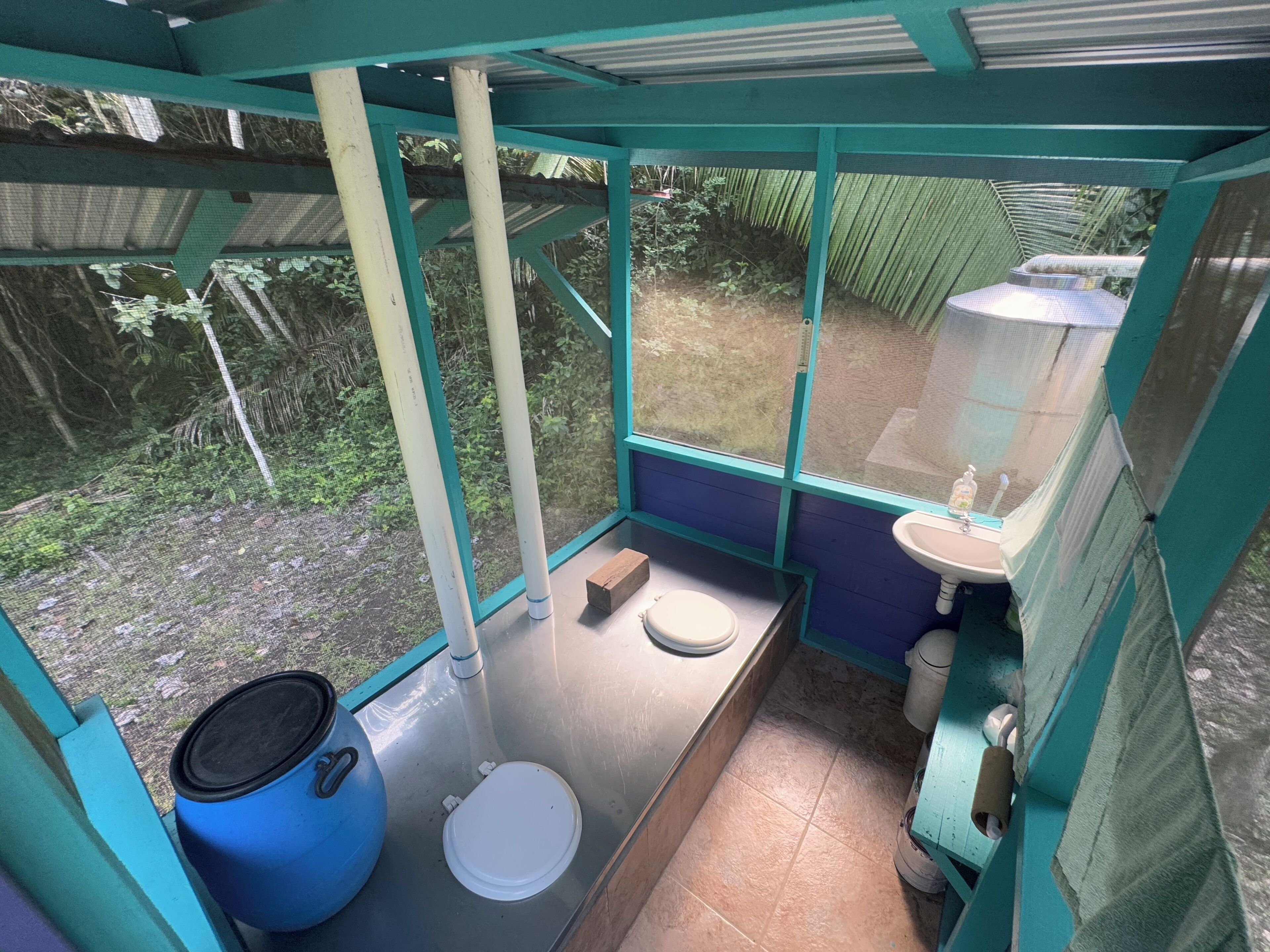 A small, enclosed bathroom with a toilet, sink, and a large blue container.