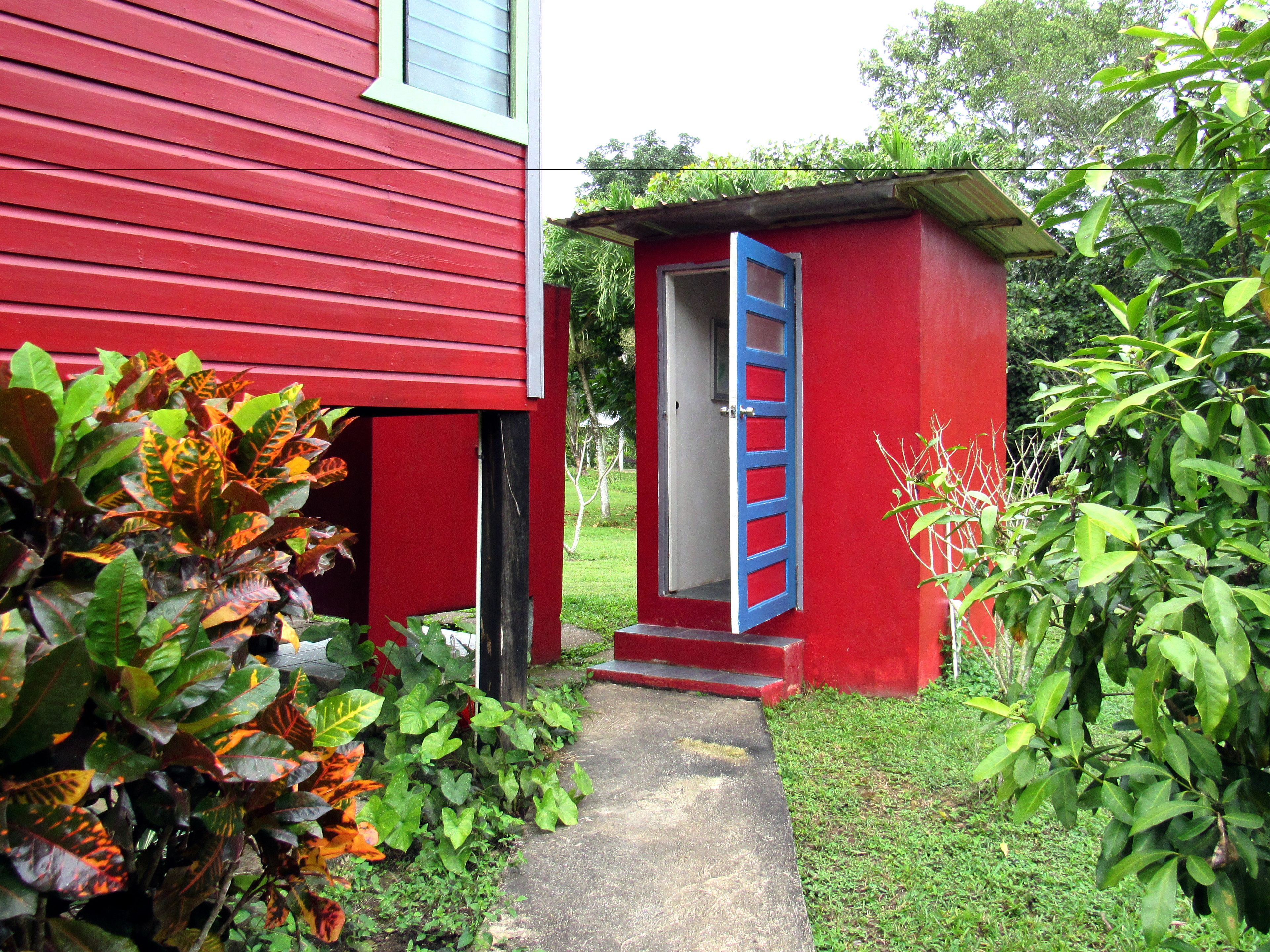 Un edificio rojo con una estructura anexa pequeña y una puerta azul.