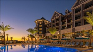 A hotel with a swimming pool, palm trees, and a sunset.