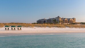 Un hôtel en bord de mer, avec plusieurs étages, une plage de sable en premier plan et un ciel dégagé.