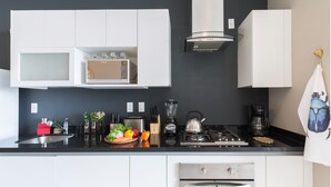 A modern kitchen with white cabinets, a black countertop, a stove, a sink, and a dishwasher. - Monet Tower By The Local Way (Mexico City)