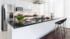 A modern kitchen with a stainless steel refrigerator, a microwave, a gas stove, and a glass island with bar stools. - Monet Tower By The Local Way (Mexico City)