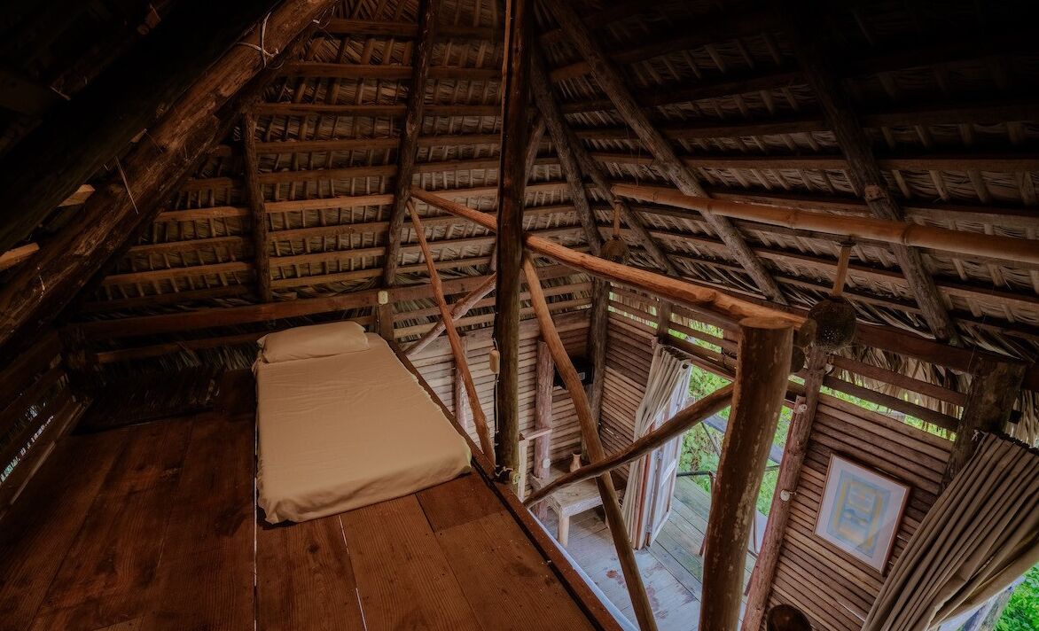 Een rustieke kamer met houten wanden, een schuine balkenlaag, een enkel bed en een klein raam.