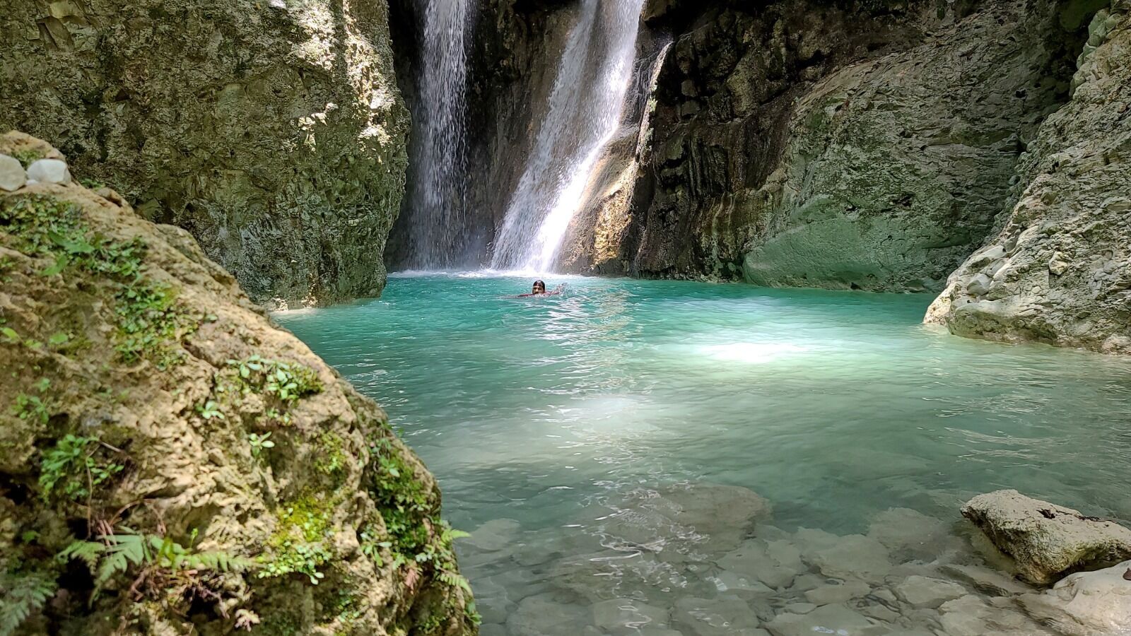 A natural pool with clear water and a waterfall.