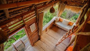 A wooden deck with a thatched roof, a cushioned seating area, and a view of greenery. - Ecolodge Tubagua Puerto Plata (Puerto Plata)