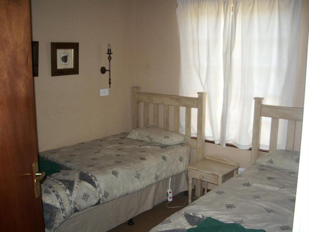 Une chambre avec deux lits simples, une petite table de chevet, une lampe fixée au mur et une fenêtre avec des rideaux.