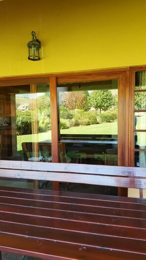 A room with a wooden bench, a yellow wall, and a view of a garden through large windows.