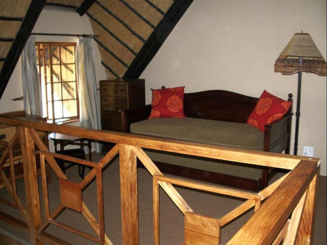 A bedroom with a wooden bed, a nightstand, a lamp, and a window with curtains.