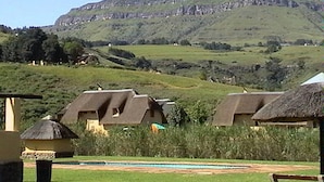 Paisaje rural con casas de campo con techos de paja, una piscina y una colina al fondo.