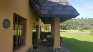 Un edificio con entrada adoquinada de piedra, un banco de madera y una mesa de picnic bajo una zona sombreada.