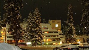 Un estacionamiento cubierto de nieve con coches y un edificio con ventanas iluminadas.
