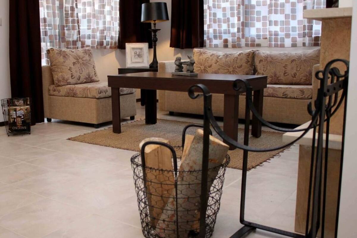 Una sala de estar con sofá, mesa de centro, lámpara y chimenea con leña.