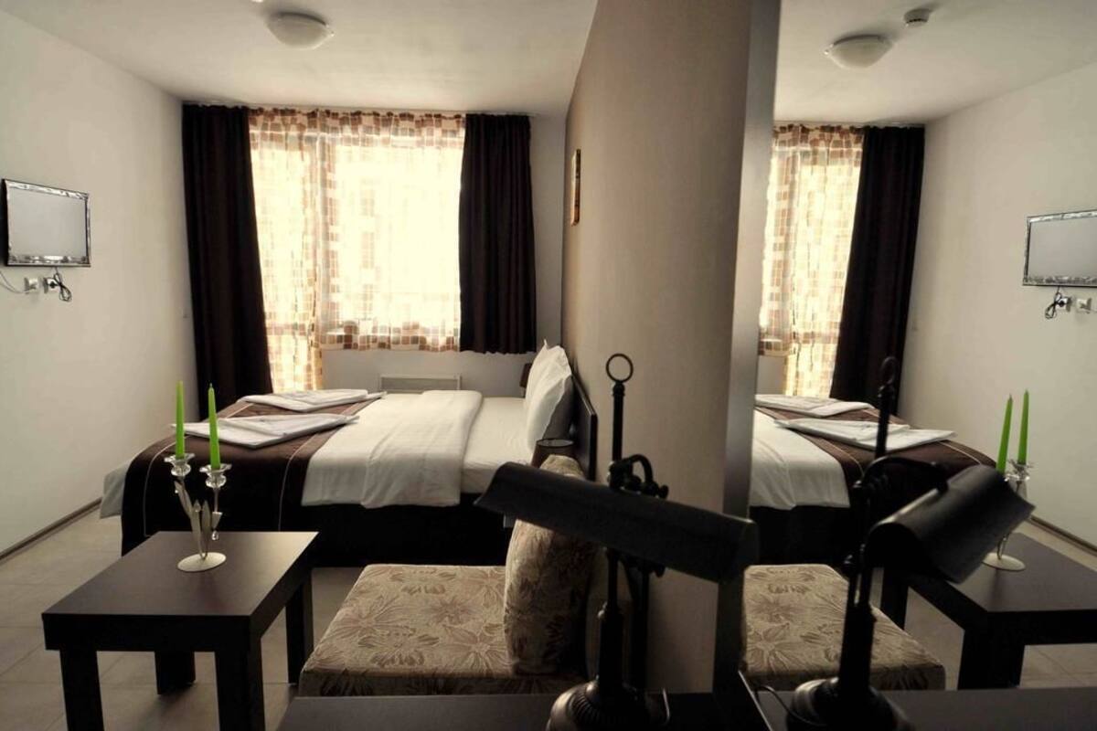 Habitación de hotel con dos camas, un escritorio, una silla, una lámpara y un televisor en la pared.