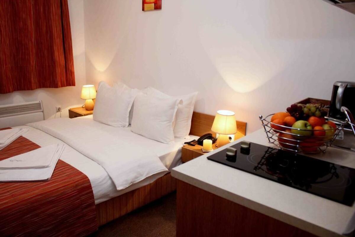 Habitación de hotel con cama, lámparas de noche, un pequeño escritorio con teléfono y frutero, y un calentador de pared.