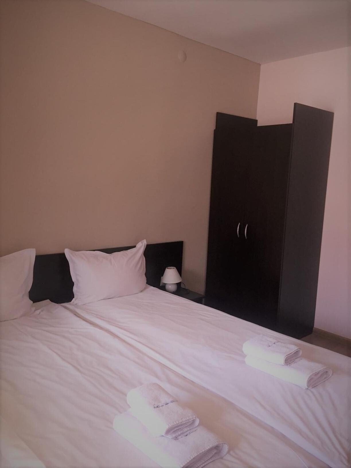 Ein Hotelzimmer mit Bett, Kissen, einem Nachttisch mit Lampe und einem dunklen Kleiderschrank.