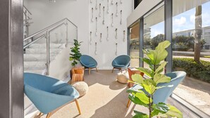 A modern interior with a staircase, blue chairs, a wall-mounted light fixture, and a large window. - Hotel Mome (San Juan)