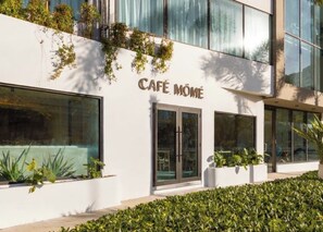 Un bâtiment avec une enseigne indiquant « CAFÉ MÔME » et de grandes fenêtres.