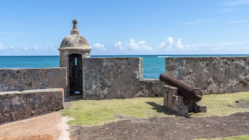 A historical fort with a cannon, a small tower, and a view of the sea.