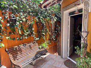 A wooden bench, a tiled patio, and a doorway leading to a room with a white door.