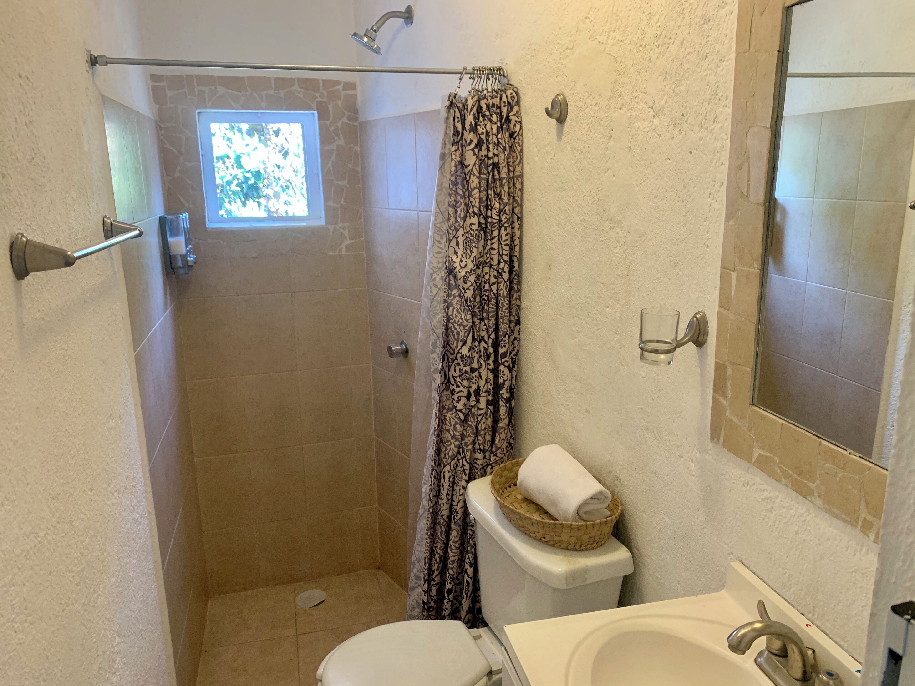 A bathroom with a shower, toilet, sink, and a small window.