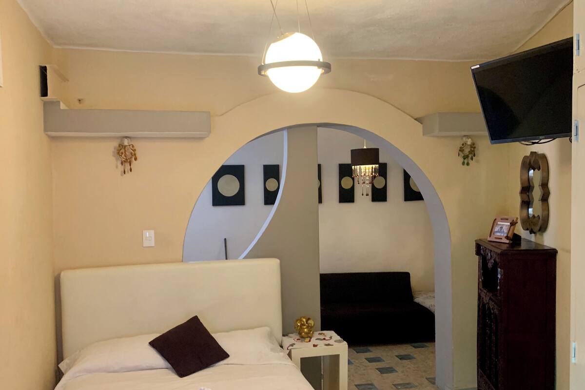 A hotel room with a bed, a small table, a TV, and a decorative mirror.