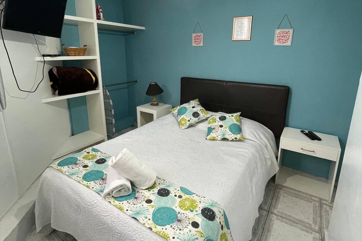 A bedroom with a bed, a nightstand, a TV on a shelf, and a ceiling fan.