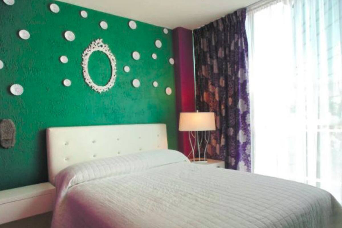 A hotel room with a bed, a nightstand, a lamp, and a window with curtains.