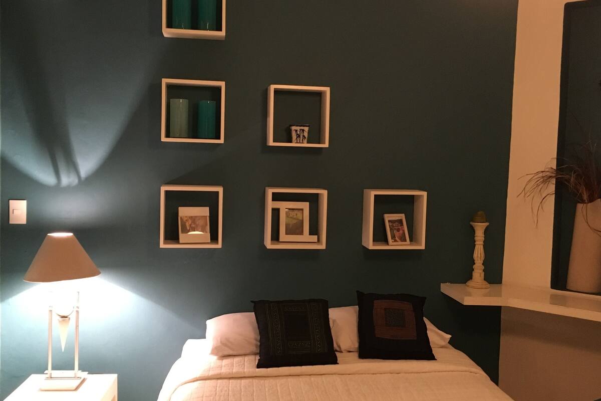 A bedroom with a bed, a nightstand, a lamp, and wall-mounted picture frames.