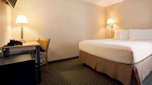 Ein Hotelzimmer mit Bett, Schreibtisch, Stuhl, Lampen und Fernseher.