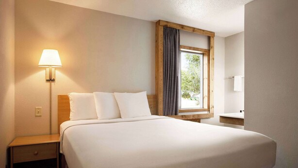 Ein Hotelzimmer mit einem großen Bett, einer Nachttischlampe, einem Fenster mit Vorhängen und einem Holz-Kopfteil.