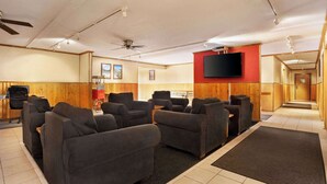 Ein Raum mit mehreren dunklen Sofas, die halbkreisförmig angeordnet sind, einem Wand-Fernseher, Deckenventilatoren und einem Holzboden.