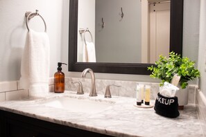 Un baño con un lavabo de mármol, un espejo grande, un perchero para toallas y una planta pequeña.